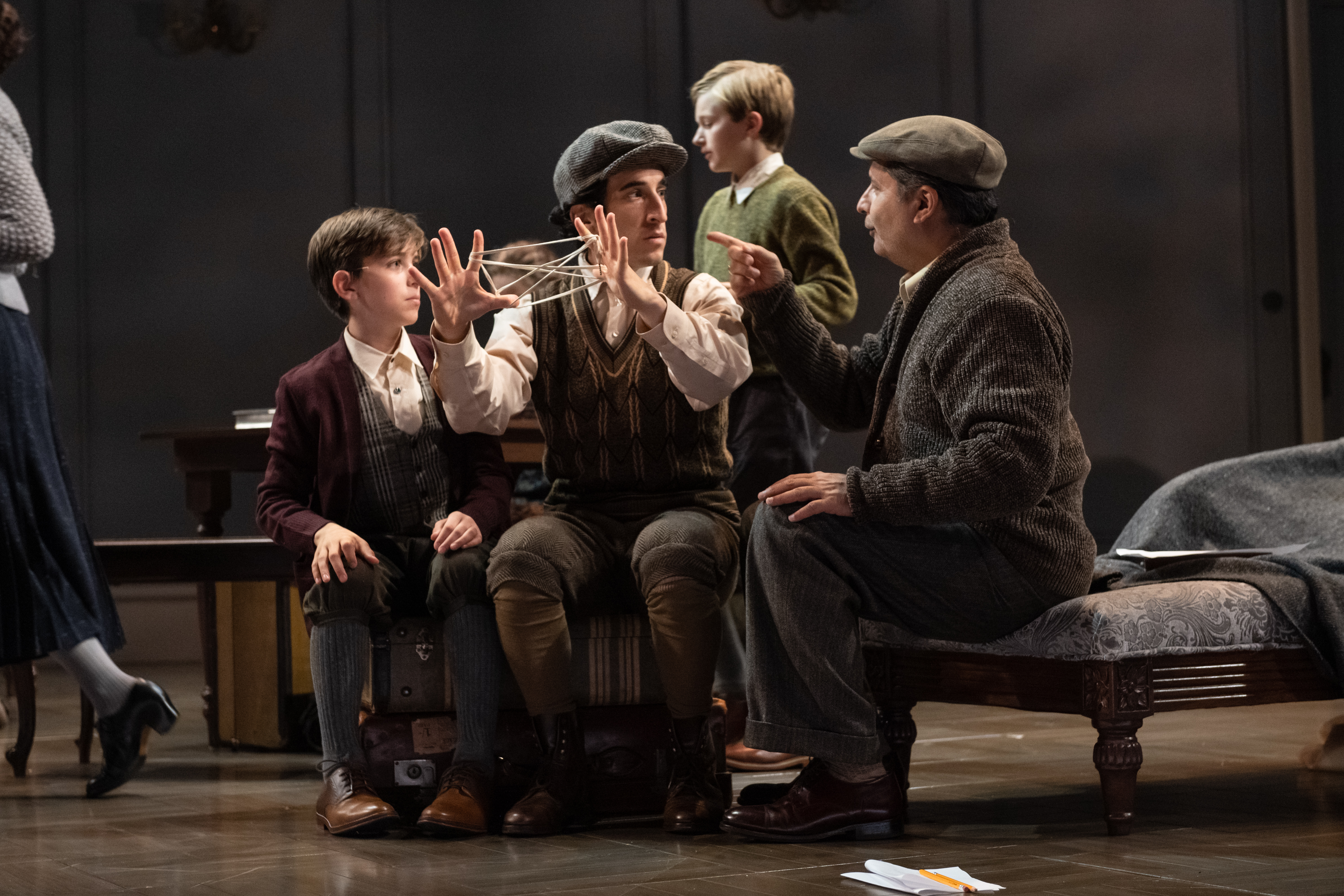 A young man and a boy playing the string game Cat's Cradle, while an older man comments.